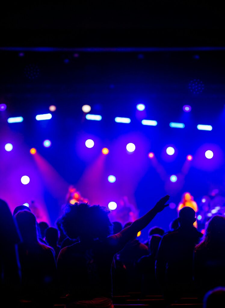 An energetic concert scene with a vibrant light show captured from the audience perspective.