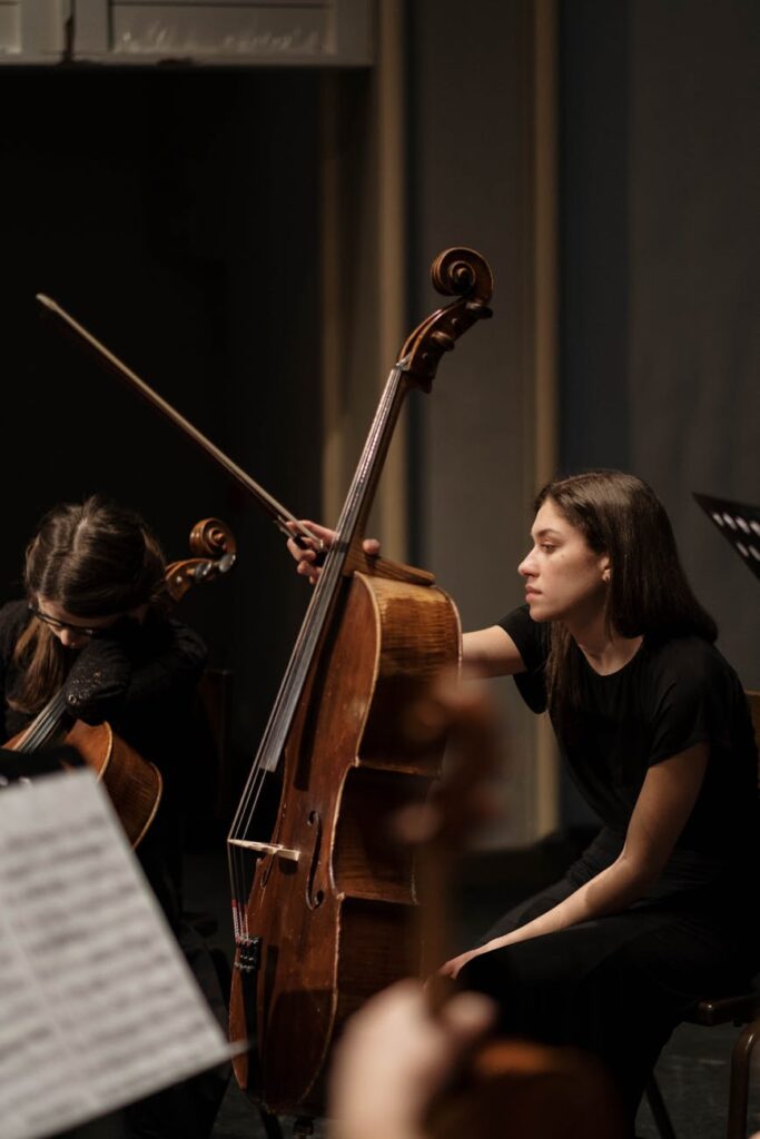 Woman playing cello during orchestra rehearsal, focusing on performance.